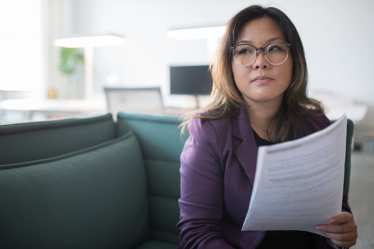 Asian businesswoman in office holding documents, expressing confidence and professionalism.